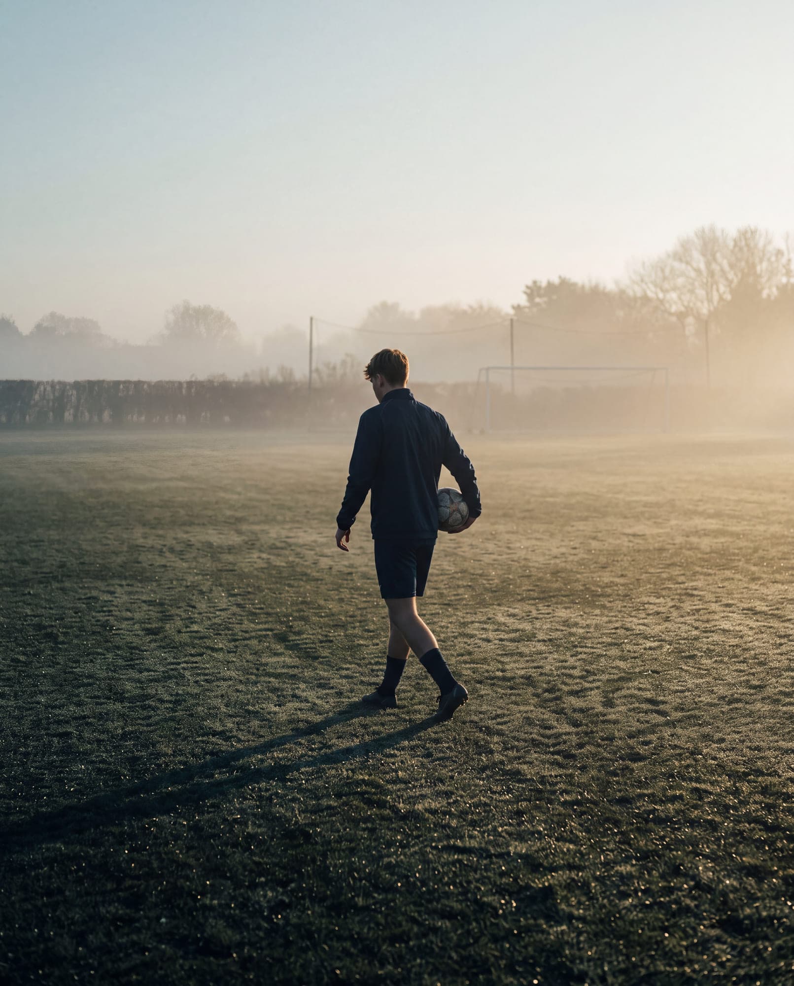 A young footballer alone on a training pitch in early morning light