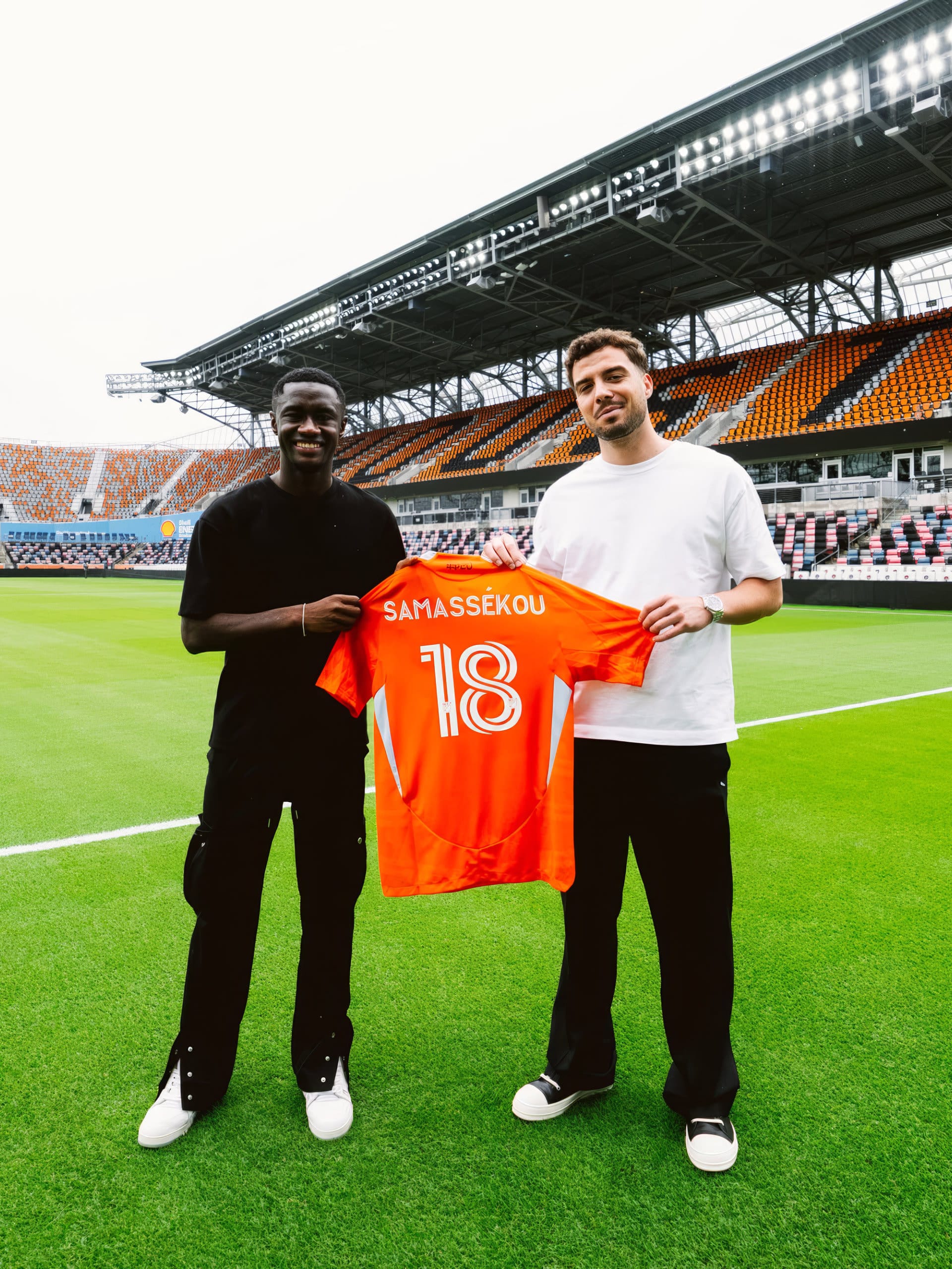 Diadié Samassékou and Felix Lang on the pitch of an empty stadium, holding an orange no. 18 shirt together