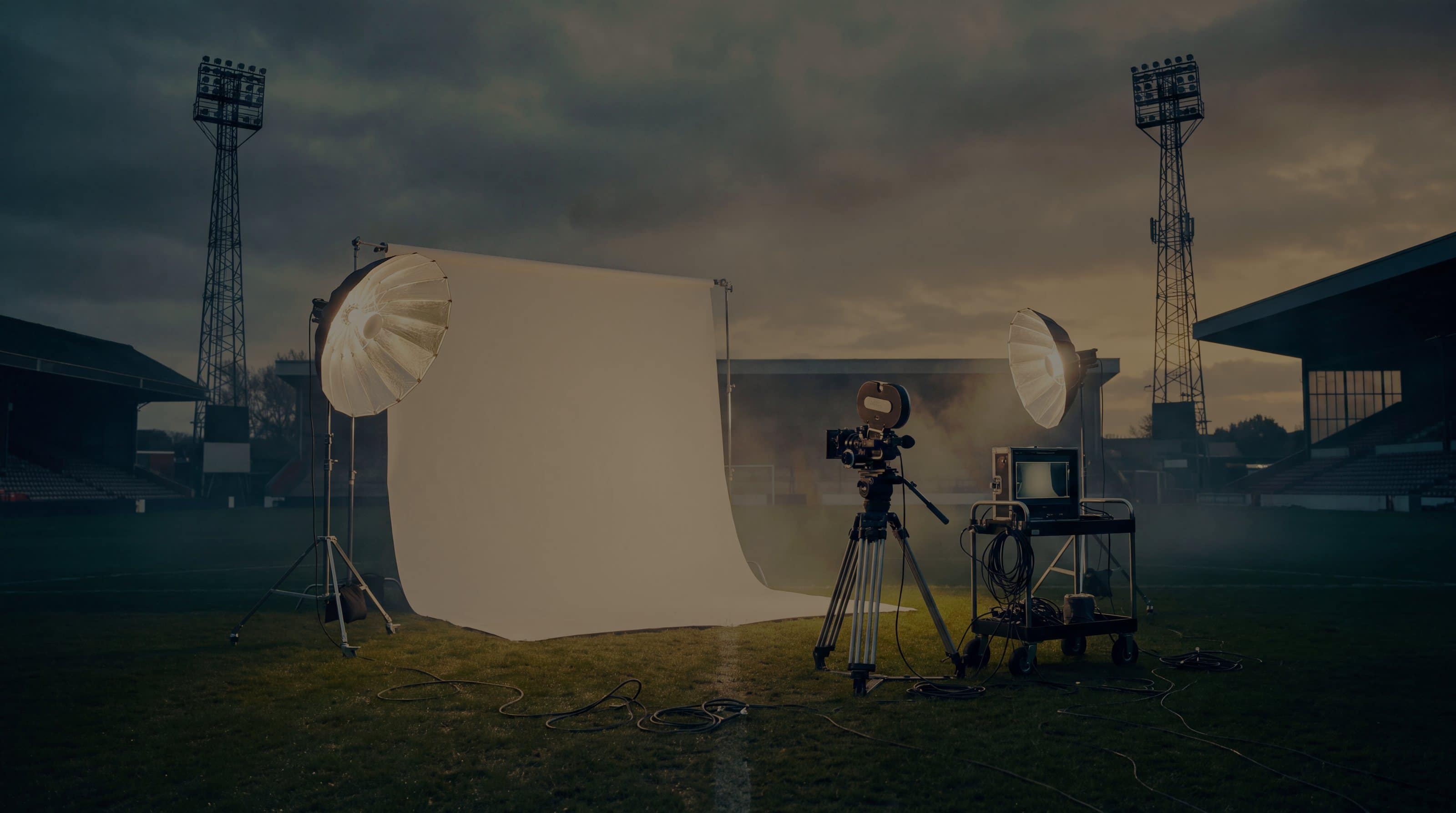 A photo studio set up on a football pitch: a paper backdrop, two lamps and a camera at dusk